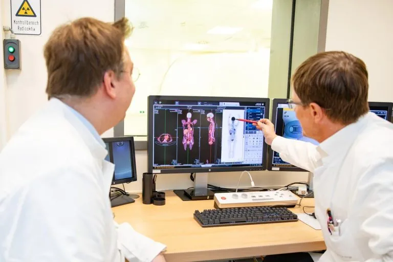 Zwei Männer in weißen Kitteln blicken auf einen Bildschirm mit Körperscans