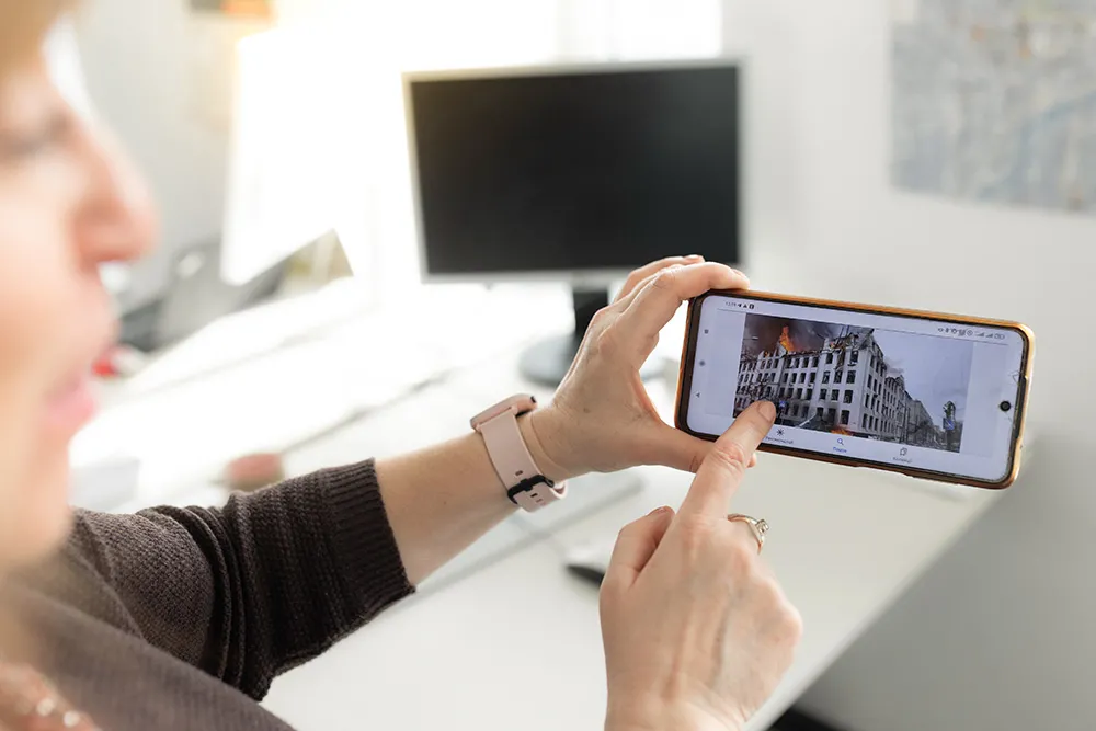 Frau zeigt ein Foto eines zerstörten Gebäudes auf dem Handy