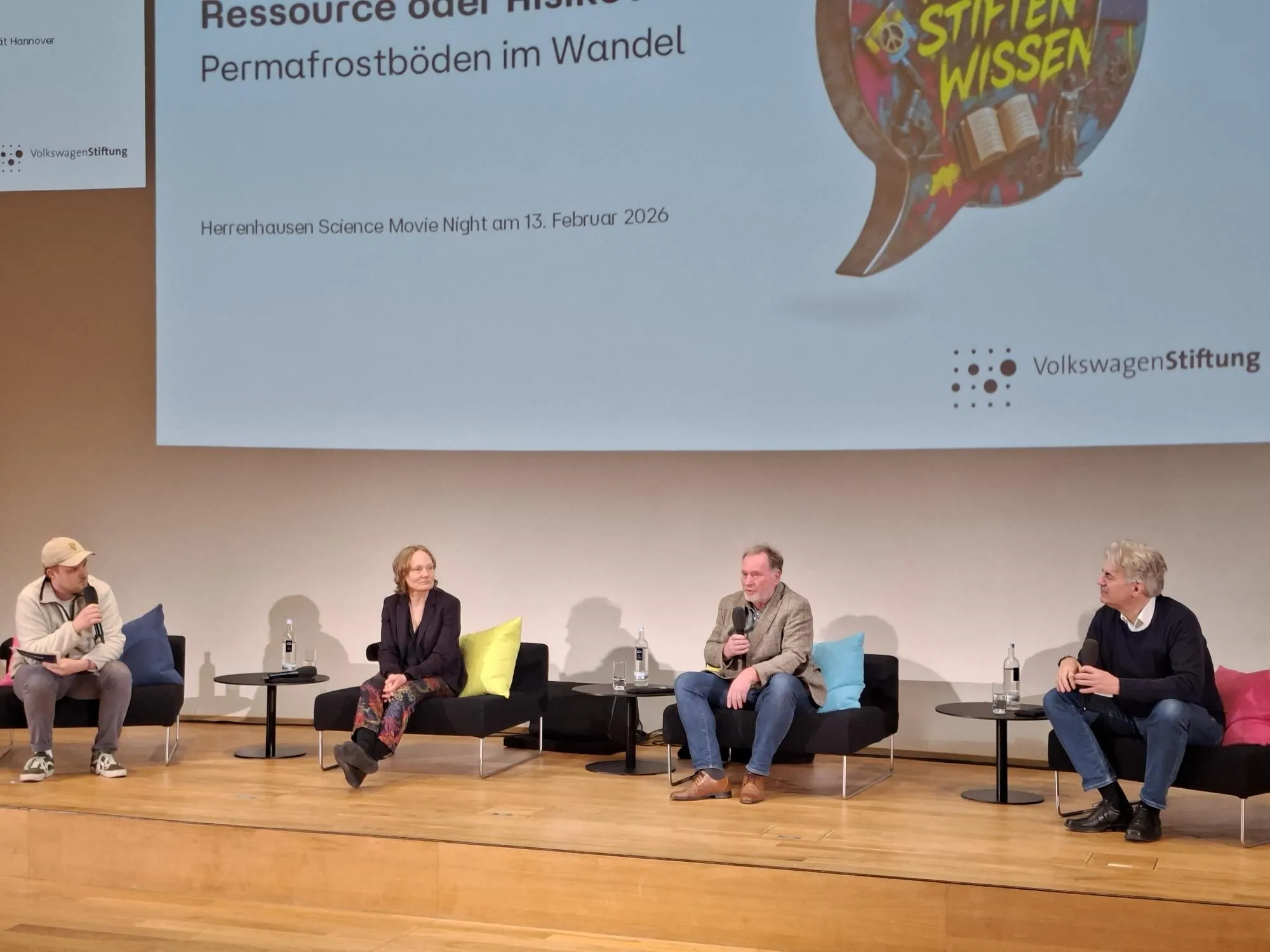 Vier Menschen auf der Bühne sitzen auf Sesseln und sprechen miteinander