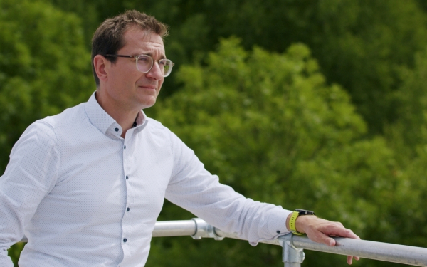 Ein Mann steht auf einer Dachterrasse und schaut in grüne Baumwipfel.