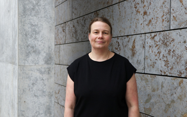 Eine Frau steht vor einer grauen Steinwand.