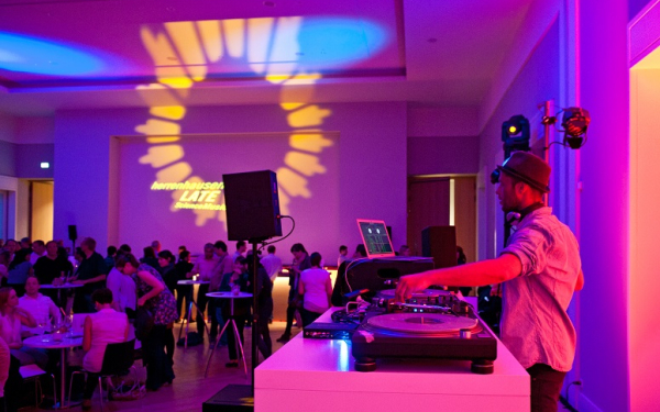 Das Bild zeigt ein Szene DJ und Publikum in loungiger Atmosphäre