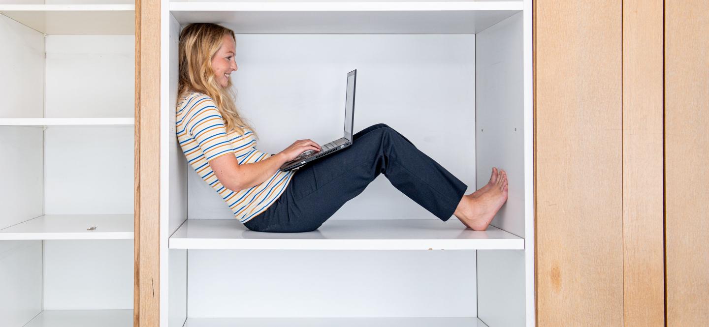 Frau mit Laptop sitzt in einem Bücherregal