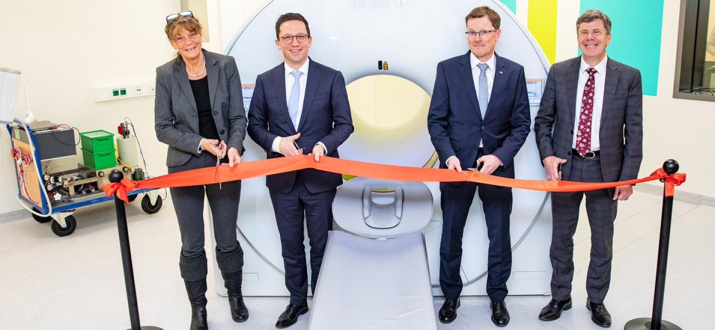 Eine Frau und drei Männer schneiden ein rotes Band durch, das vor einer großen weißen Röhre steht