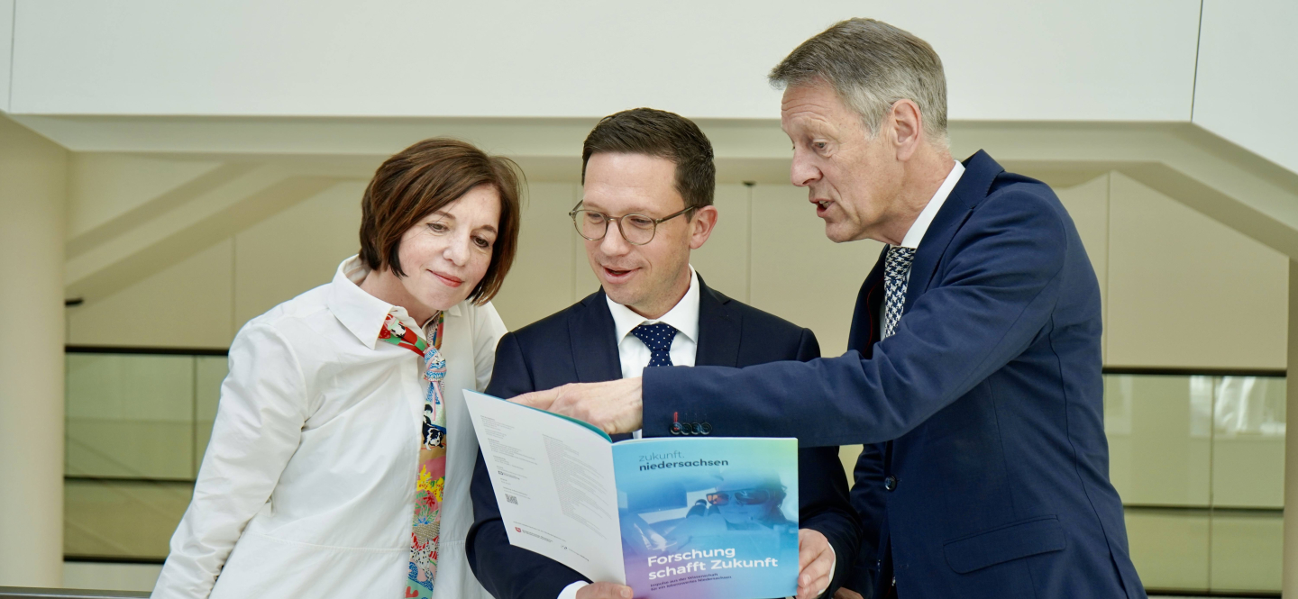 Eine Frau und zwei Männer sehen gemeinsam in ein buntes Heft