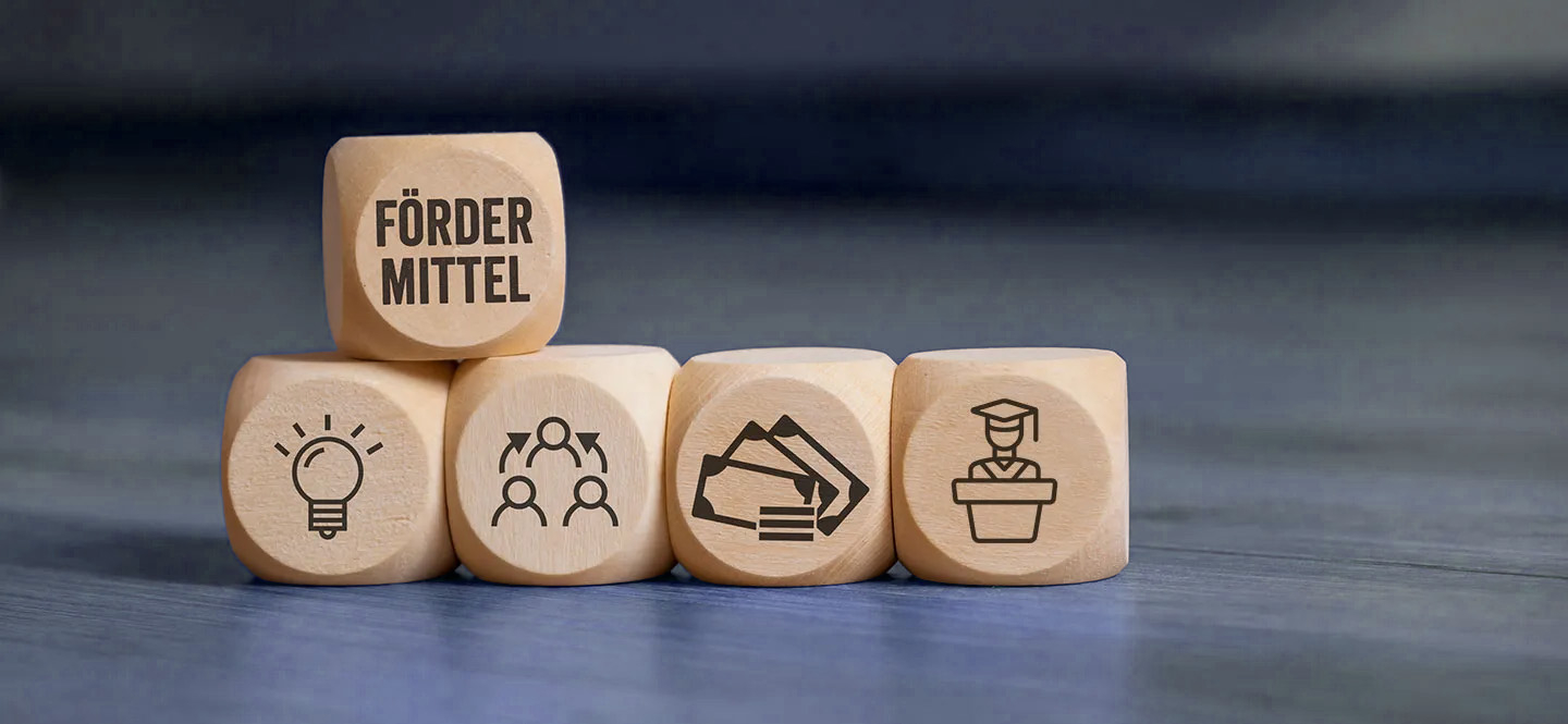 mehrere Würfel mit Symbolen, darunter einer mit der Aufschrift Fördermittel