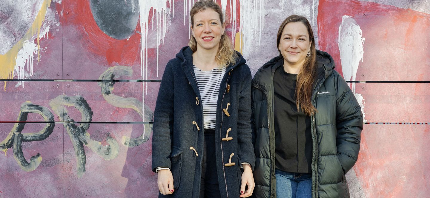 Zwei Frauen stehen nebeneinander vor einer bunten Wand