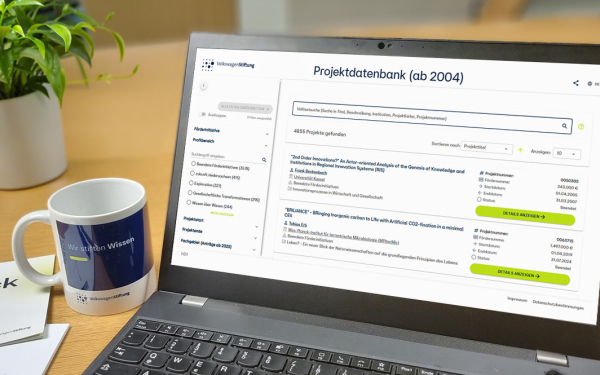 Schreibtisch mit Laptop mit geöffneter Seite "Projektdatenbank", Tasse, Flyer "Steckbrief" und Pflanze