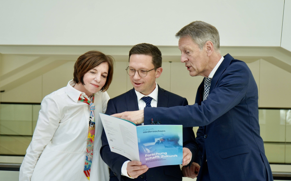 Eine Frau und zwei Männer sehen gemeinsam in ein buntes Heft