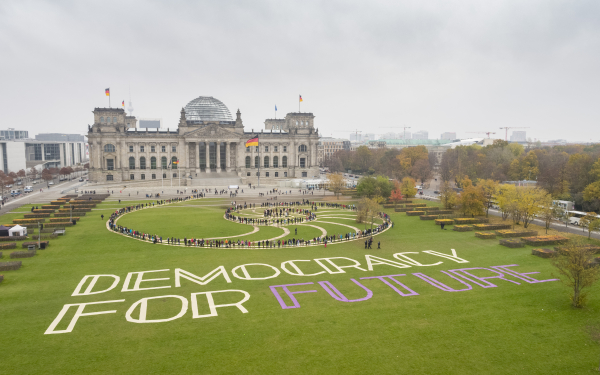 In einer Kunstaktion stehen Menschen auf einer Fibonacci-Folge auf der Wiese vor dem Reichstagsgebäude in Berlin