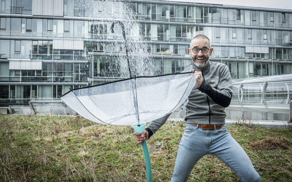 Das Bild zeigt Prof. Köster, der den Regen mit einem Schirm auffängt und in einer grünen Dachfläche speichert.