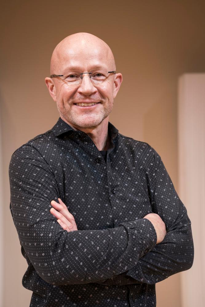 Ein Mann mit Brille schaut in die Kamera und lächelt.