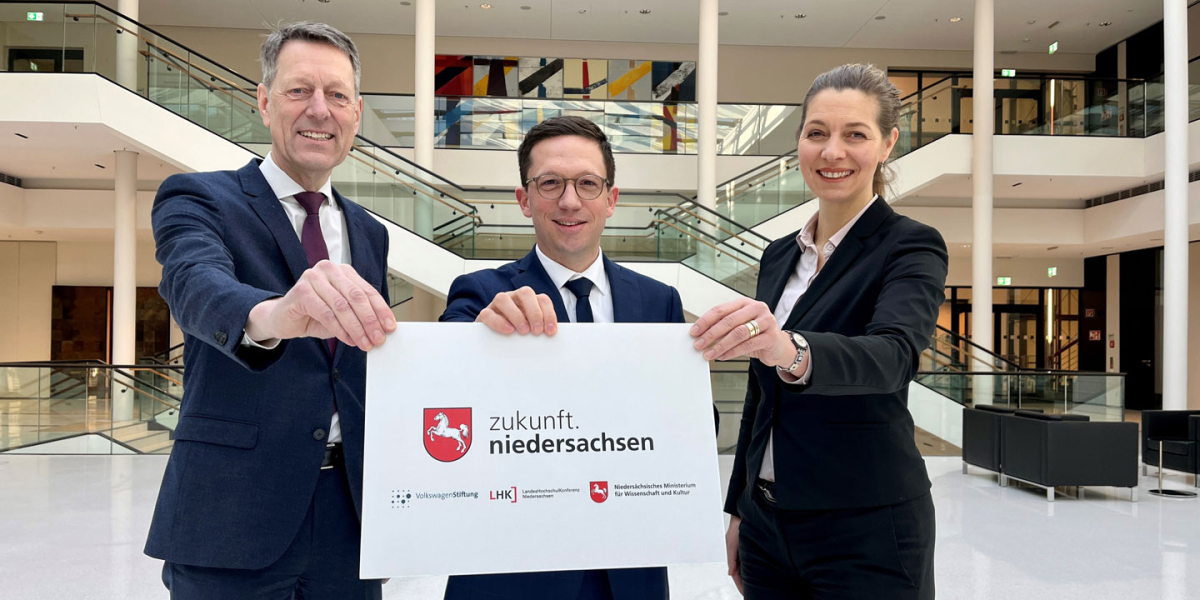 Zwei Männer und eine Frau halten ein Schild mit dem Aufdruck "zukunft.niedersachsen" in die Kamera