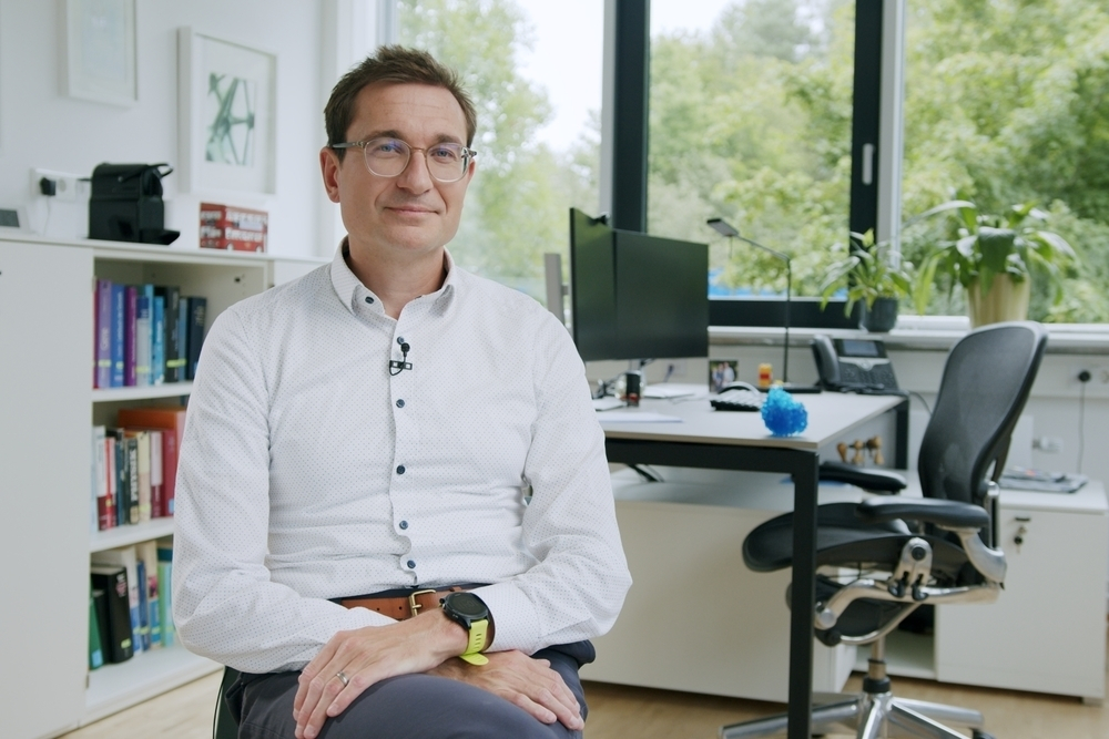 Ein Mann sitzt in einem Büro und schaut in die Kamera.