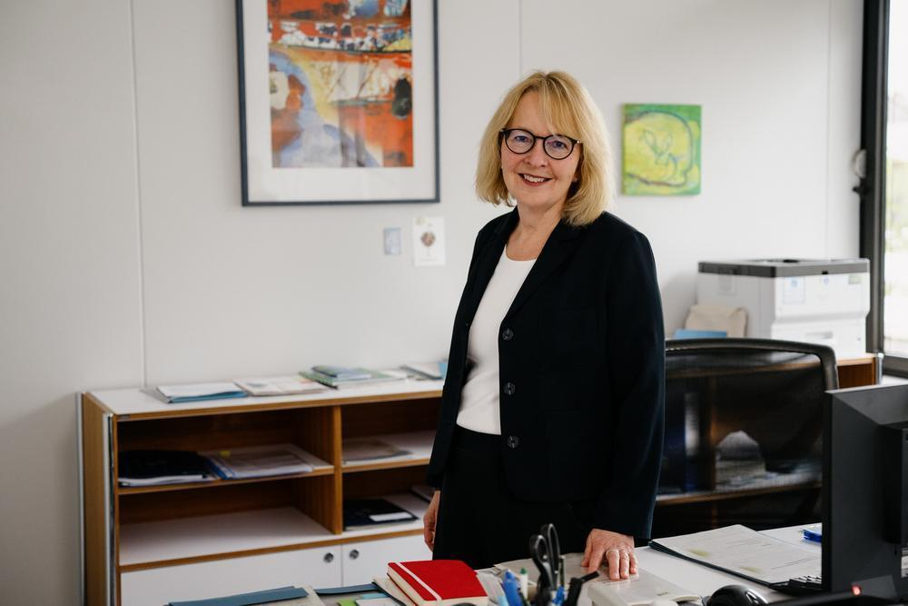 Eine Frau steht in einem Büro und schaut in die Kamera.