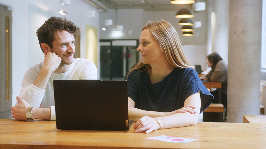 Ein Mann und eine Frau unterhalten sich vor Laptop.