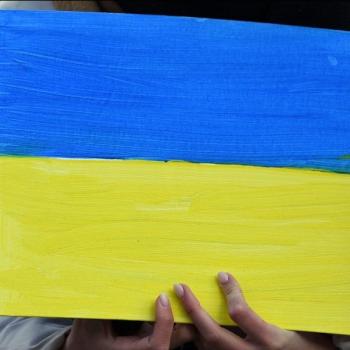 Eine Hand hält ein Plakat mit der gemalten Ukraine Flagge