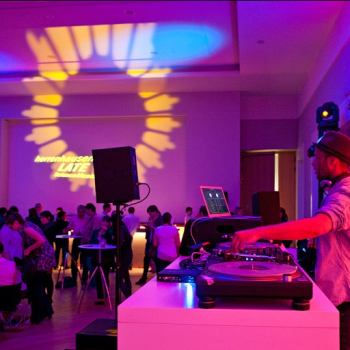 Das Bild zeigt eine Szene mit DJ und Publikum in loungiger Atmosphäre