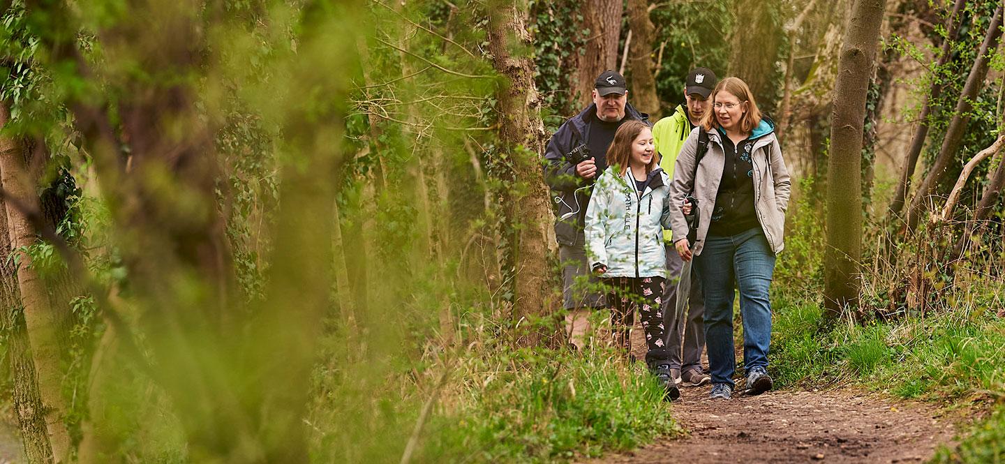 Eine Frau und ein Mädchen laufen vor einem Mann und einem Jugendlichen durch den Wald.