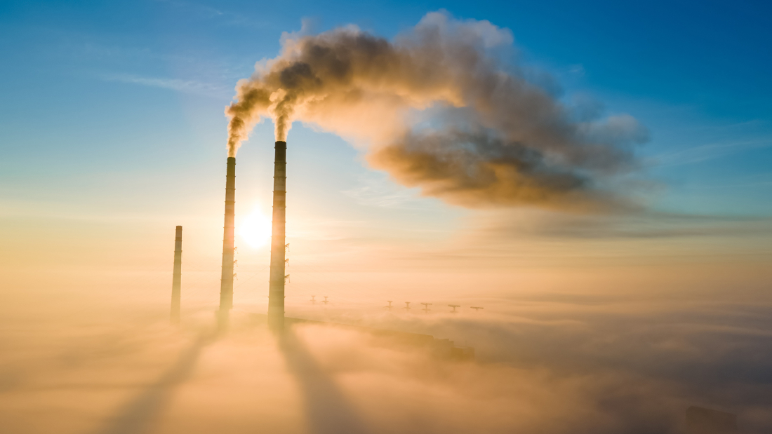 Das Bild zeigt Industrieschorsteine, aus denen Dampf kommt, vor einem Sonnenaufgang.
