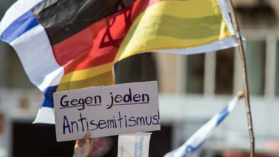 Das Bild zeigt ein Pappschild mit dem Schriftzug "Gegen jeden Antisemitismus" vor einer Deutschland- und einer Israelflagge