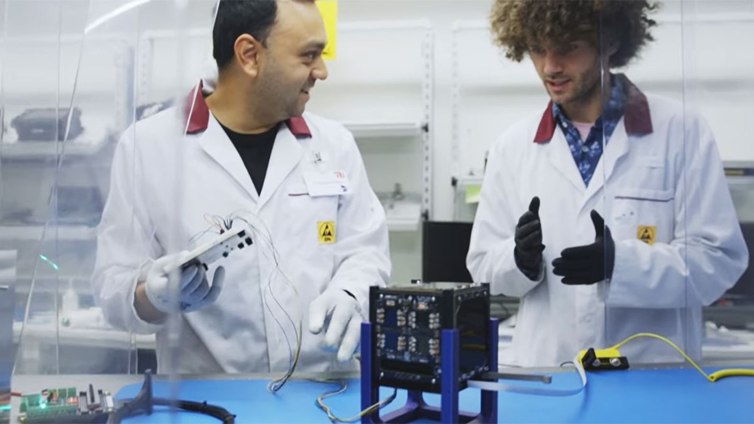 Zwei Männer vor einem würfelförmigen Satelliten. 